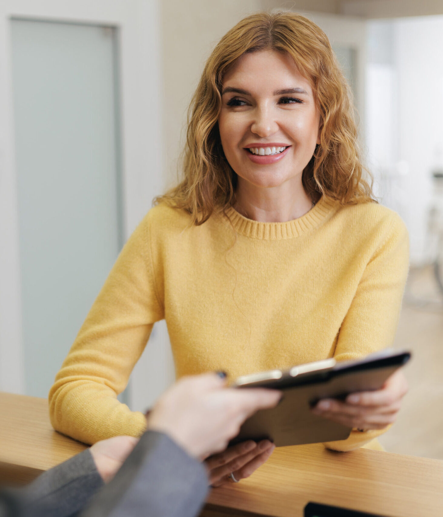 Smiling caucasian female adult with folder for papers at reception desk of clinic.